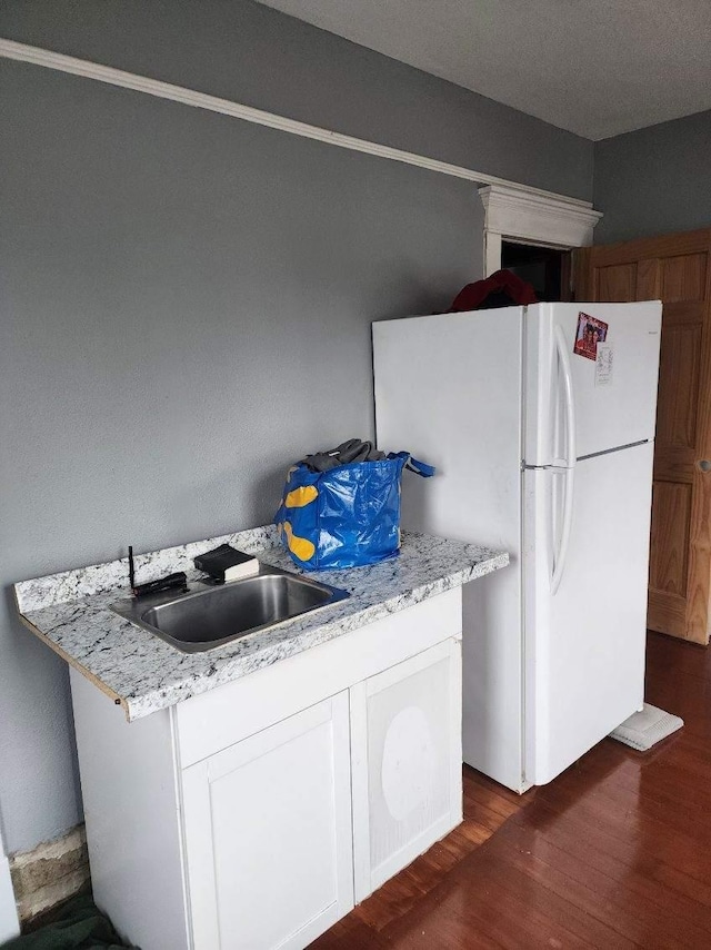 kitchen featuring white cabinets, white refrigerator, sink, dark hardwood / wood-style floors, and light stone countertops