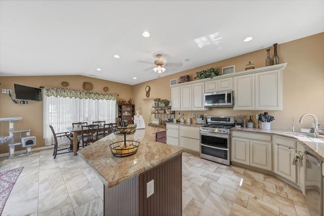 kitchen featuring sink, a center island, stainless steel appliances, light stone counters, and lofted ceiling