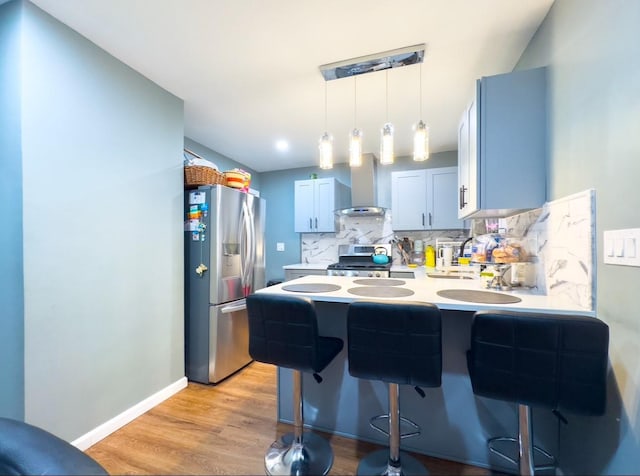 kitchen with hanging light fixtures, wall chimney exhaust hood, appliances with stainless steel finishes, tasteful backsplash, and a kitchen bar