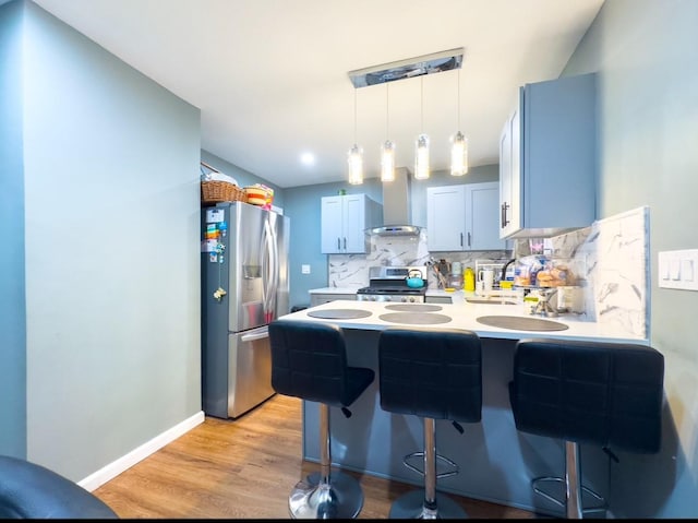 kitchen featuring wall chimney range hood, appliances with stainless steel finishes, tasteful backsplash, decorative light fixtures, and a kitchen bar