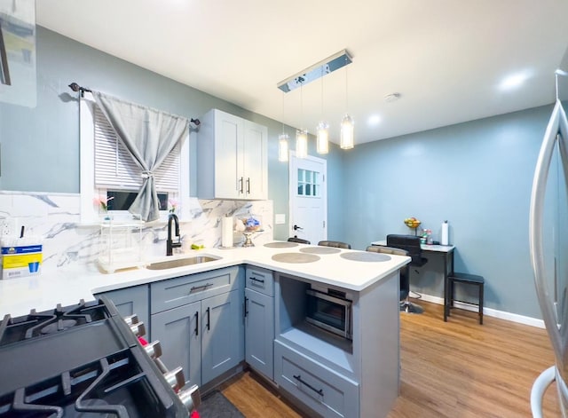 kitchen with sink, hanging light fixtures, hardwood / wood-style flooring, decorative backsplash, and kitchen peninsula