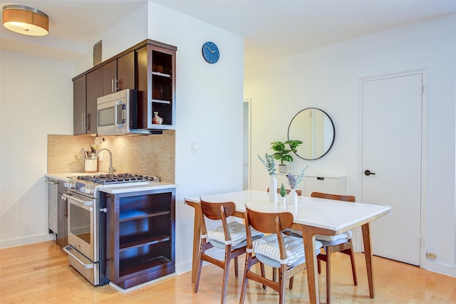 kitchen featuring decorative backsplash, appliances with stainless steel finishes, dark brown cabinetry, and light hardwood / wood-style flooring