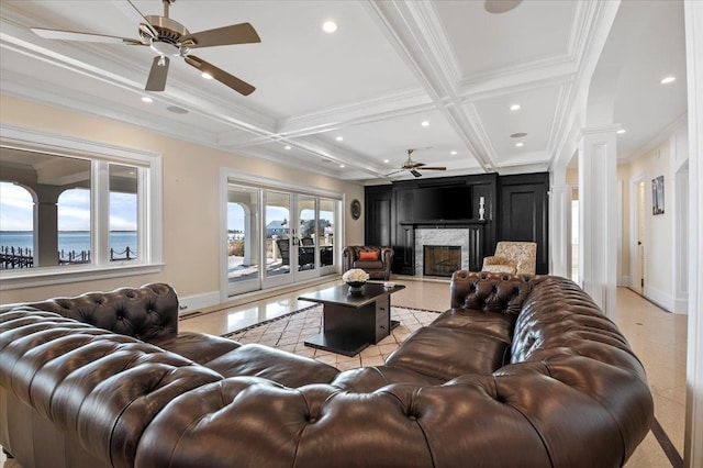 living room featuring ornate columns, coffered ceiling, a stone fireplace, beamed ceiling, and a water view