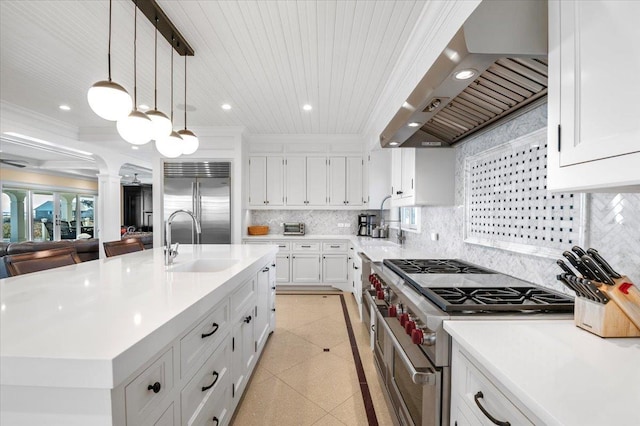 kitchen featuring sink, wall chimney exhaust hood, premium appliances, pendant lighting, and a center island with sink