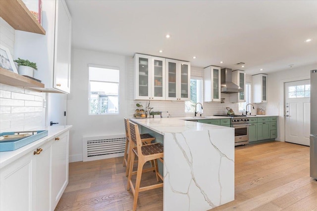 kitchen with high end stove, white cabinetry, and wall chimney exhaust hood