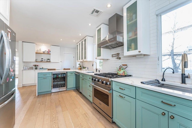 kitchen with wall chimney range hood, light hardwood / wood-style flooring, white cabinetry, stainless steel appliances, and beverage cooler