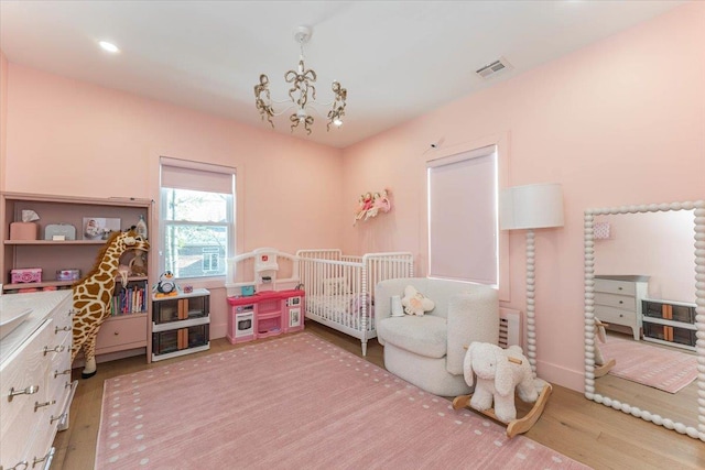 bedroom featuring wood-type flooring, a crib, and a chandelier