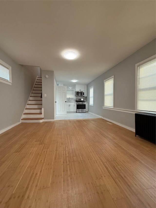 unfurnished living room featuring radiator heating unit and light hardwood / wood-style flooring