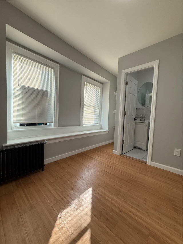 empty room featuring radiator heating unit, sink, and light hardwood / wood-style flooring