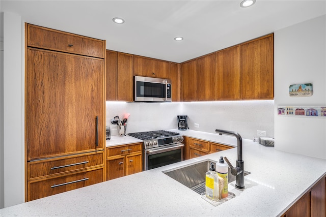 kitchen with light stone counters, stainless steel appliances, kitchen peninsula, and sink