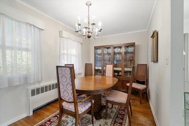 dining area with hardwood / wood-style floors, ornamental molding, radiator, and an inviting chandelier