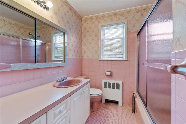 full bathroom featuring radiator heating unit, combined bath / shower with glass door, toilet, vanity, and ornamental molding