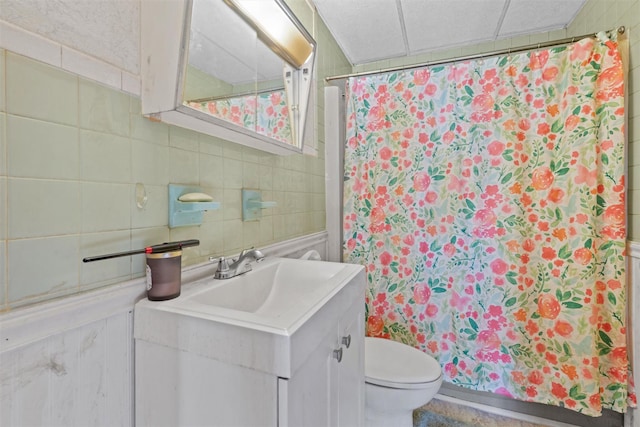 bathroom featuring toilet, a drop ceiling, walk in shower, and vanity