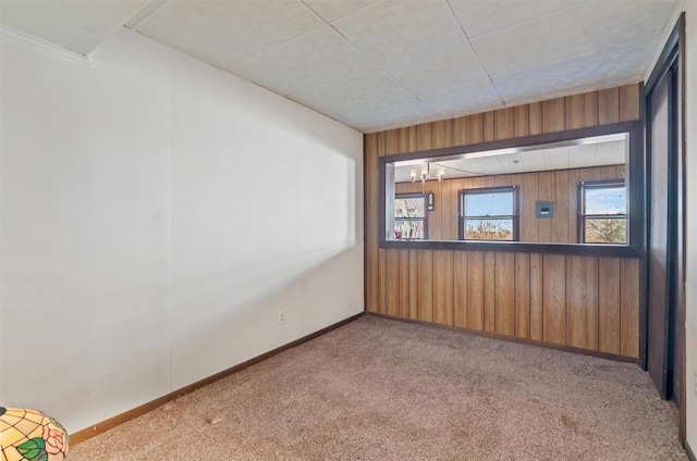 spare room with an inviting chandelier, wood walls, and light carpet