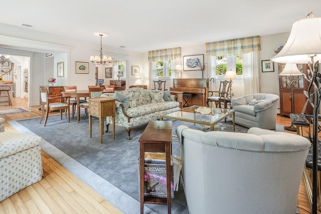 living room with plenty of natural light, wood finished floors, visible vents, and an inviting chandelier