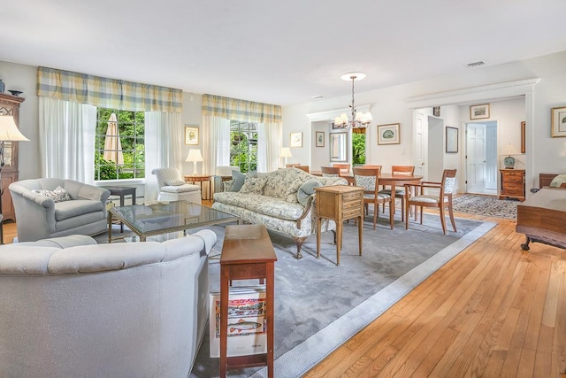 living room featuring light wood-style flooring, visible vents, and a notable chandelier