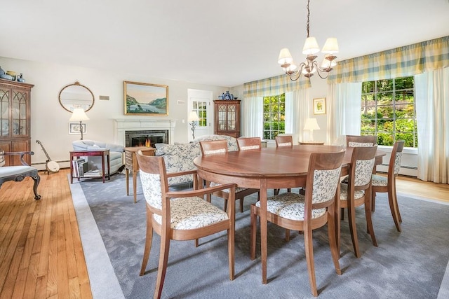 dining space with a baseboard heating unit, an inviting chandelier, a lit fireplace, and light wood finished floors