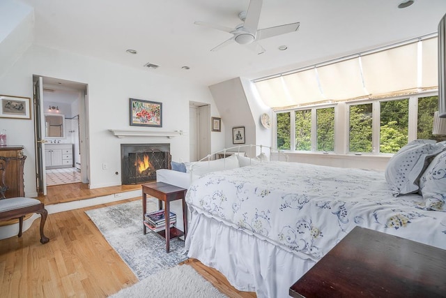 bedroom featuring wood finished floors, a warm lit fireplace, baseboards, visible vents, and recessed lighting
