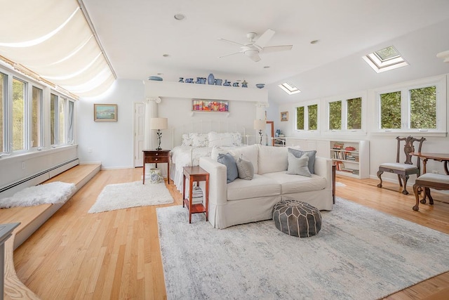 interior space with a baseboard radiator, a ceiling fan, vaulted ceiling with skylight, wood finished floors, and baseboards