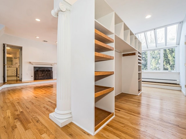 walk in closet with a baseboard heating unit, decorative columns, visible vents, a fireplace with raised hearth, and wood finished floors