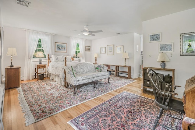 bedroom with wood finished floors, visible vents, a ceiling fan, and baseboard heating