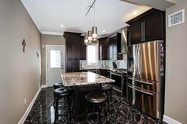 kitchen with appliances with stainless steel finishes, wall chimney range hood, a kitchen island, light stone counters, and a breakfast bar area