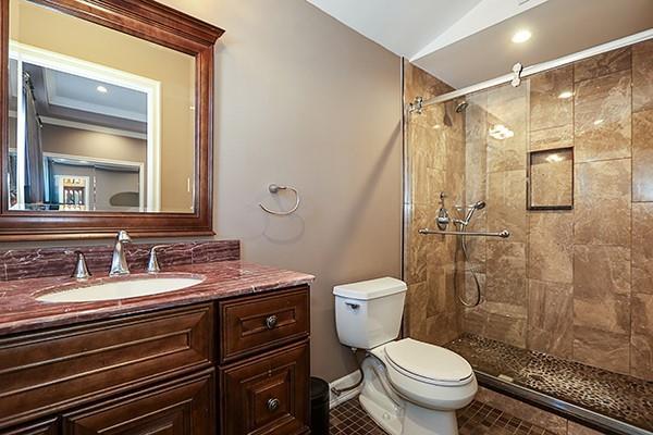 bathroom featuring lofted ceiling, tile patterned floors, vanity, toilet, and tiled shower