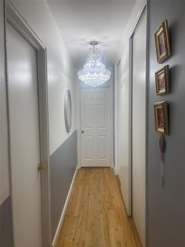 corridor with an inviting chandelier, ornamental molding, and light hardwood / wood-style flooring