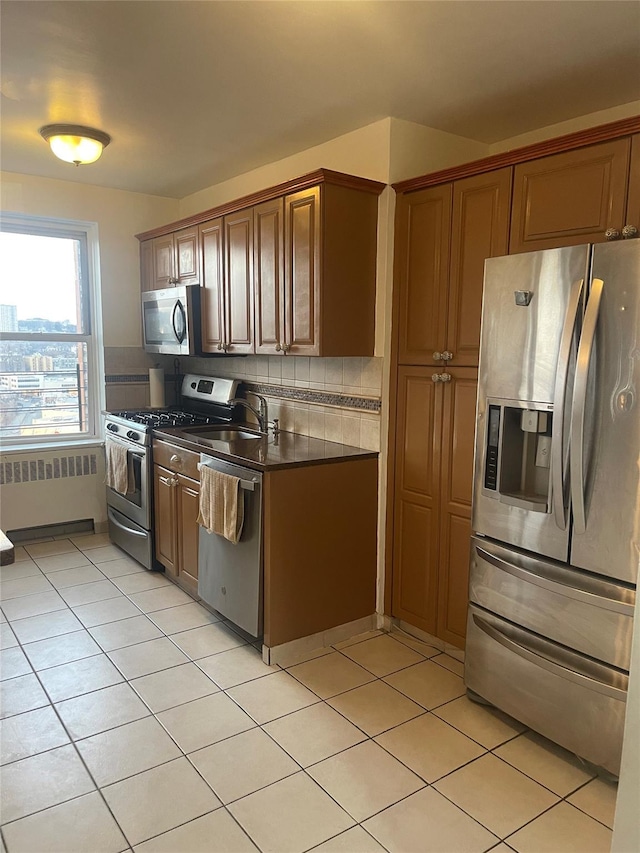 kitchen featuring radiator, backsplash, light tile patterned flooring, and appliances with stainless steel finishes