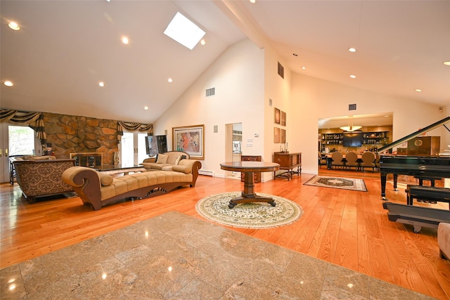 living room featuring hardwood / wood-style flooring, a stone fireplace, high vaulted ceiling, and a skylight