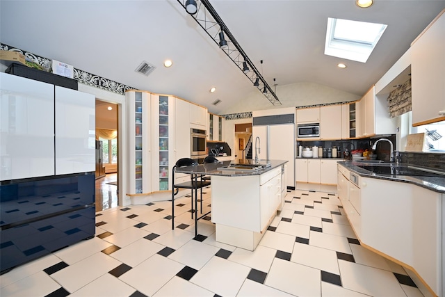 kitchen with backsplash, white cabinets, vaulted ceiling with skylight, built in appliances, and a kitchen island