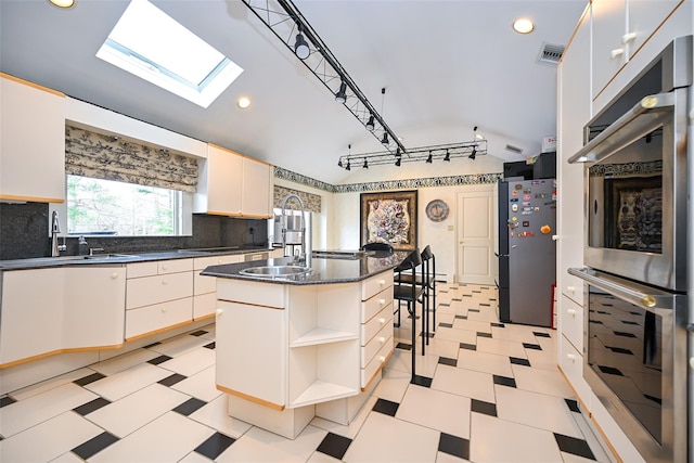 kitchen with sink, backsplash, a kitchen island with sink, vaulted ceiling with skylight, and appliances with stainless steel finishes