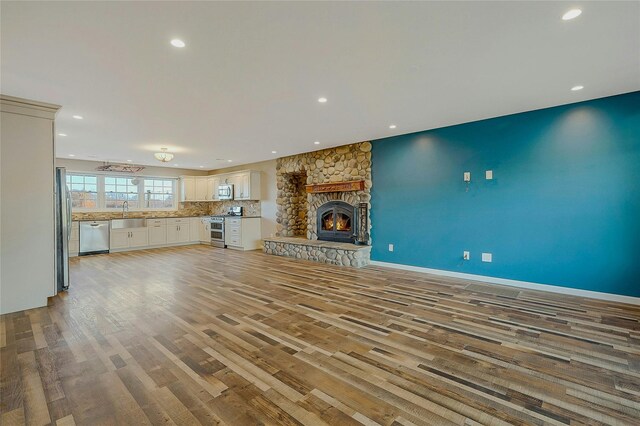 unfurnished living room featuring a stone fireplace, sink, and light hardwood / wood-style flooring