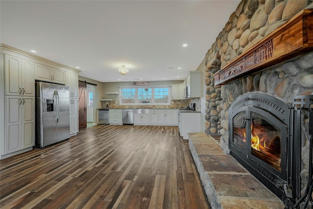 kitchen featuring dark wood-type flooring, a fireplace, appliances with stainless steel finishes, tasteful backsplash, and white cabinetry