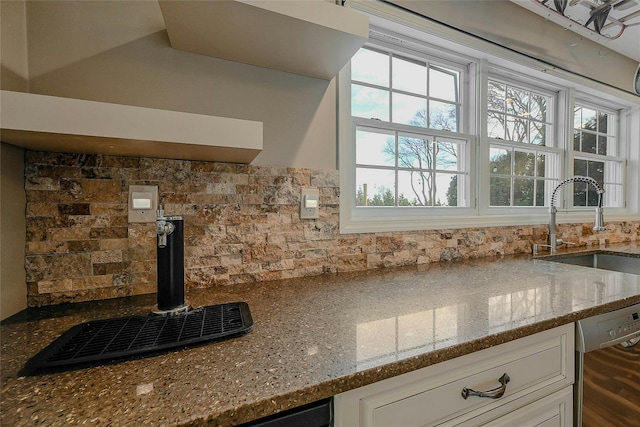 kitchen with stainless steel dishwasher, white cabinetry, light stone countertops, and sink