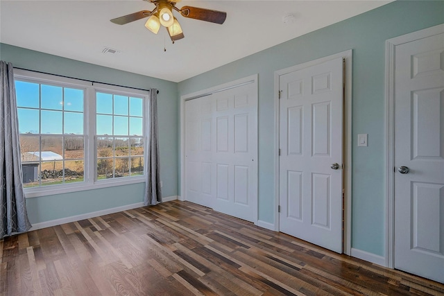 unfurnished bedroom with ceiling fan, dark hardwood / wood-style flooring, and two closets