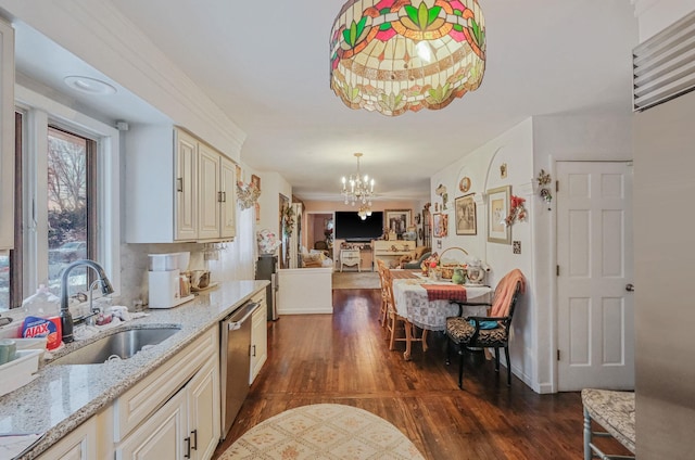 kitchen with sink, stainless steel dishwasher, light stone counters, an inviting chandelier, and cream cabinetry