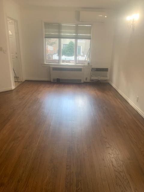 spare room with a wall mounted air conditioner, radiator heating unit, and dark hardwood / wood-style floors