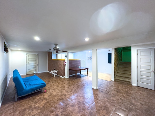 living area with ceiling fan and brick wall