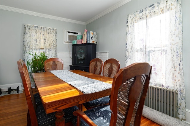 dining space with radiator, wood-type flooring, a wall mounted air conditioner, and ornamental molding