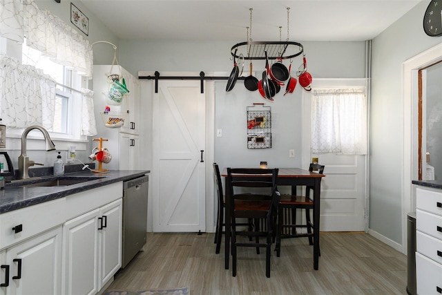 kitchen with white cabinets, sink, stainless steel dishwasher, a barn door, and light hardwood / wood-style floors