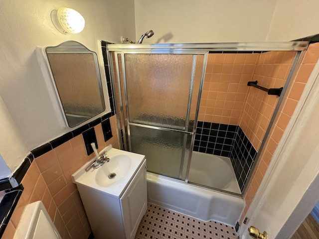 bathroom featuring vanity, bath / shower combo with glass door, and tile walls