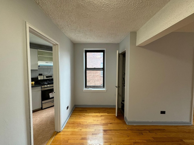 corridor with a textured ceiling and light hardwood / wood-style flooring