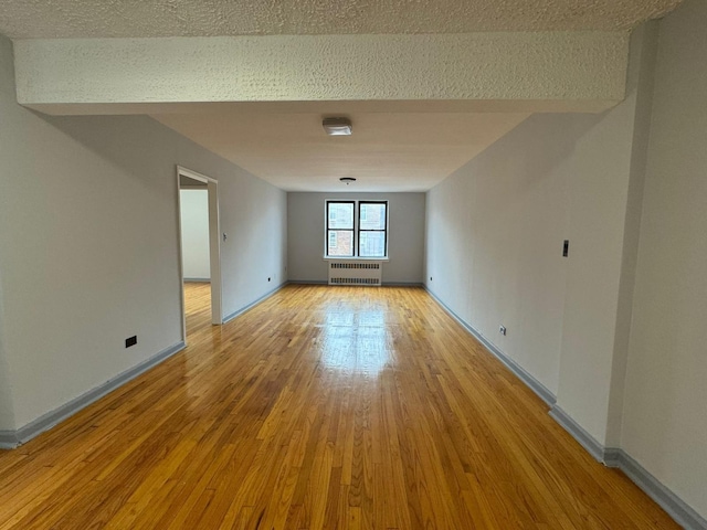 empty room with radiator heating unit, light hardwood / wood-style floors, and a textured ceiling