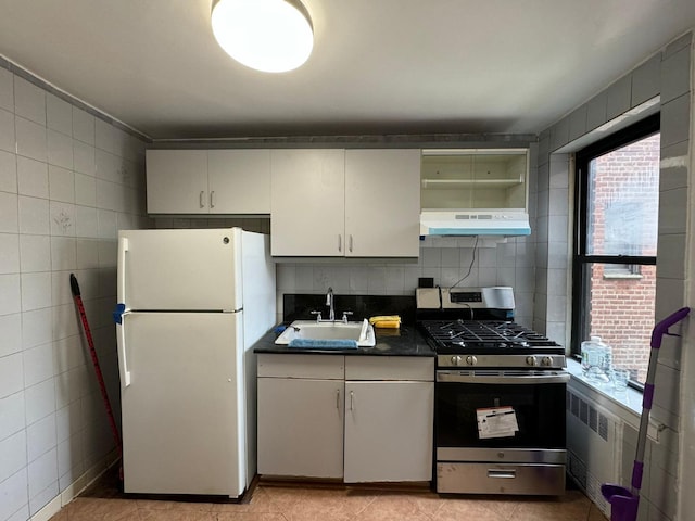 kitchen featuring stainless steel range with gas cooktop, sink, radiator heating unit, white fridge, and white cabinetry