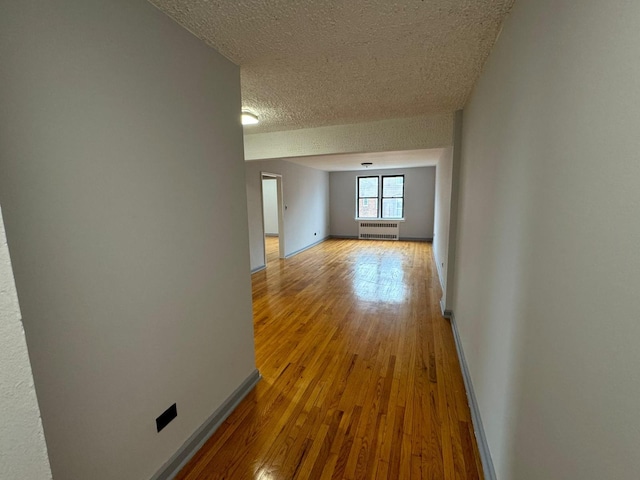 hallway featuring radiator heating unit, a textured ceiling, and light hardwood / wood-style floors