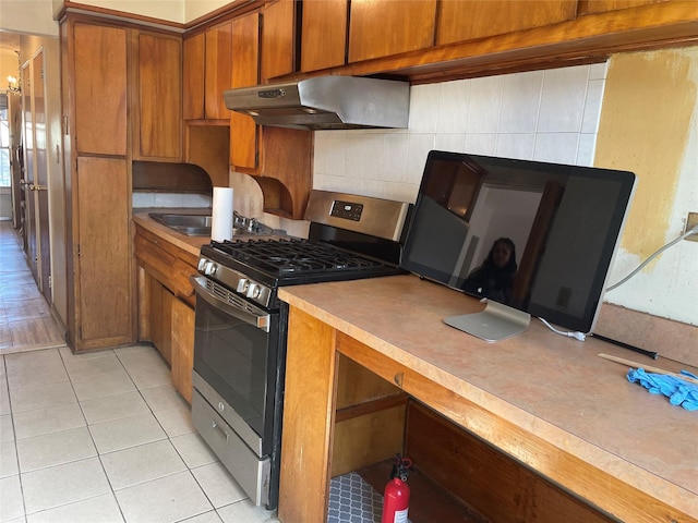 kitchen featuring under cabinet range hood, light tile patterned floors, brown cabinetry, and gas stove