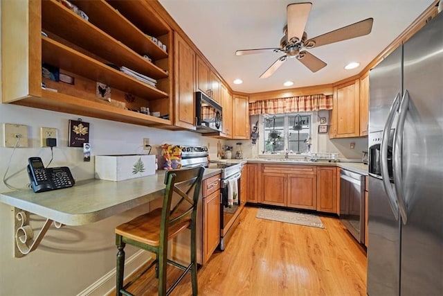 kitchen with appliances with stainless steel finishes, a breakfast bar, ceiling fan, sink, and light hardwood / wood-style floors