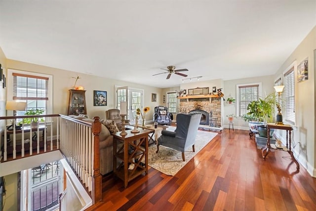 living room featuring ceiling fan, a stone fireplace, dark wood-type flooring, and a wealth of natural light