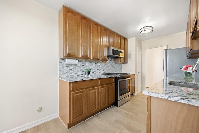 kitchen with light stone countertops, appliances with stainless steel finishes, tasteful backsplash, sink, and light hardwood / wood-style floors